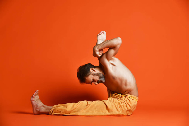 Old man practicing yoga doing stretching exercises against orange background - Фото, изображение