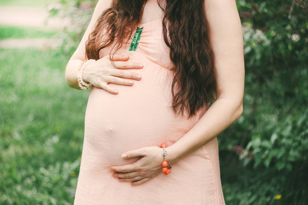 Περικοπή φωτογραφία του έγκυος γυναίκα με μακριά σκούρα μαλλιά σε φόντο πράσινο άνθιση φύση - Φωτογραφία, εικόνα