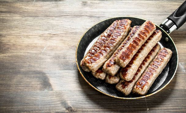 Fried sausages in a frying pan. On a wooden table. - Photo, Image