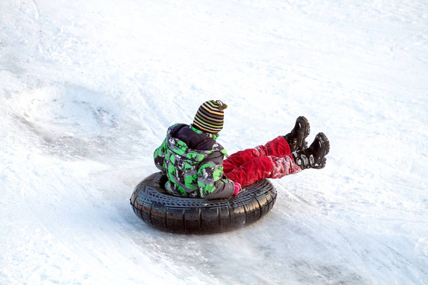 glücklicher Junge mit Schneeschlauch. Winterspaß. Rutschen den Hügel hinunter auf einer Schneeröhre - Foto, Bild