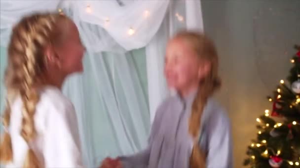 Retrato em câmera lenta de duas garotas rindo com tranças e de camisola de mãos dadas, pulando na cama e olhando uma para a outra - Filmagem, Vídeo