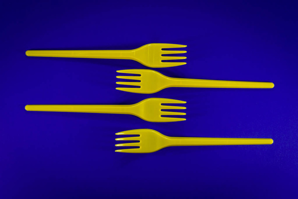 Arrangesd πλαστικά πιρούνια μαχαιροπίρουνα κίτρινο σε μπλε φόντο. Πρόβλημα των πλαστικών αποβλήτων πρωτότ - Φωτογραφία, εικόνα