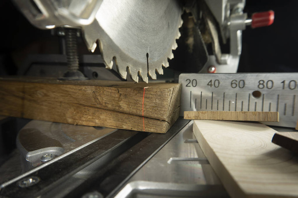 Dents sur une scie circulaire en gros plan avec des blocs de bois assortis et une balance métallique pour couper les longueurs dans un atelier de menuiserie
 - Photo, image