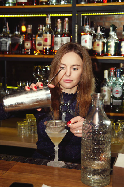 Professional bartender girl pouring a delicious cocktail into the glass at bar counter - Photo, image
