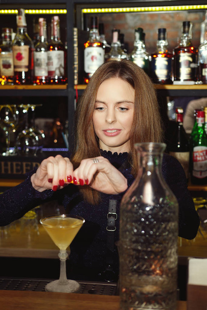 Professional bartender girl squeezing a orange peel in cocktail - Photo, image