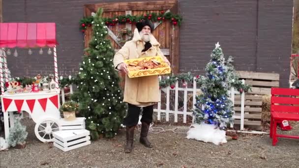 Sliding view of white bearded old man in overcoat and hat selling homemade cracknels at Christmas fair - Footage, Video