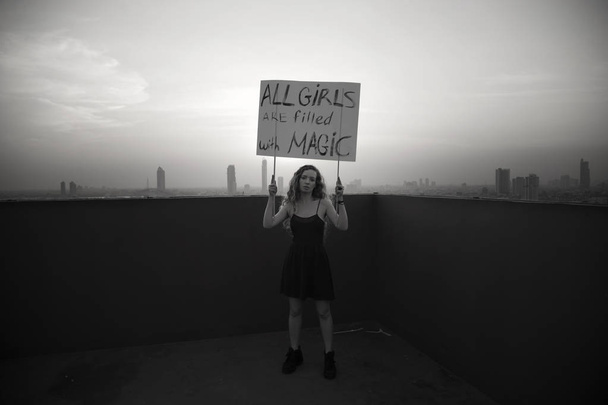 The girl stands on the roof with a poster "All girls are filled with Magic" International Womens Day concept - Photo, Image