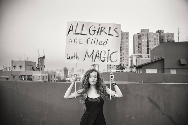 Το κορίτσι στέκεται στη στέγη με μια αφίσα της έννοιας «όλα τα κορίτσια είναι γεμάτο μαγεία» διεθνής ημέρα γυναικών - Φωτογραφία, εικόνα
