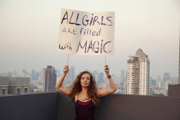 La chica se para en el techo con un póster "Todas las niñas están llenas de magia" Día Internacional de la Mujer concepto
 - Foto, Imagen