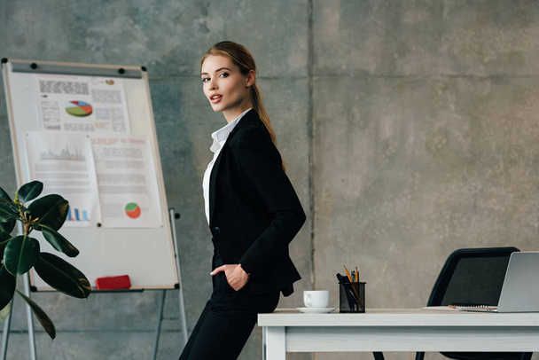 beautiful businesswoman standing by desk with hands in pockets - Fotografie, Obrázek