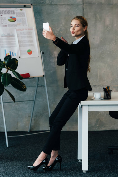 young businesswoman standing by work desk and taking selfie with duck face - Foto, imagen