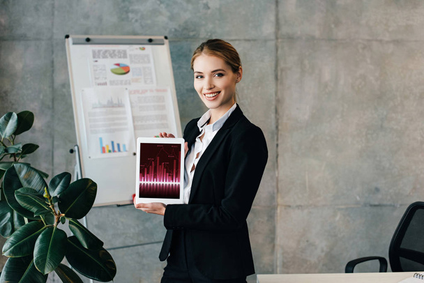 Jolie femme d'affaires souriante tenant une tablette numérique avec des graphiques à l'écran
 - Photo, image
