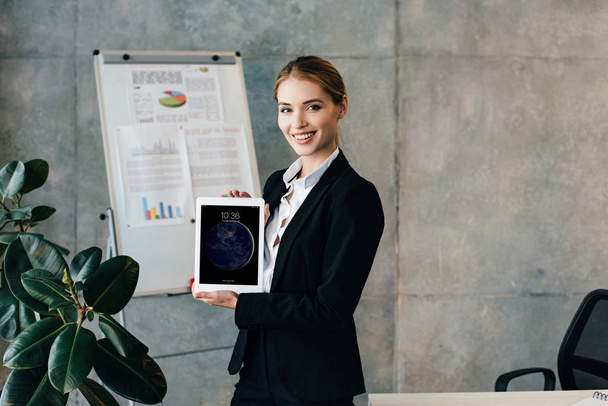 Beautiful smiling businesswoman showing ipad screen and looking at camera in office - Foto, Imagem