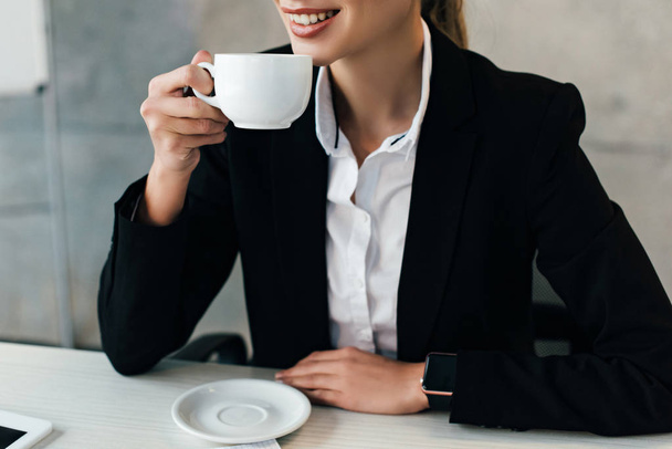 Teilbild einer lächelnden Geschäftsfrau, die am Arbeitsplatz im Büro Kaffee trinkt - Foto, Bild