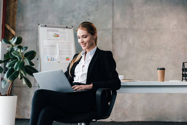 Smiling pretty businesswoman sitting on chair and using laptop - Фото, изображение