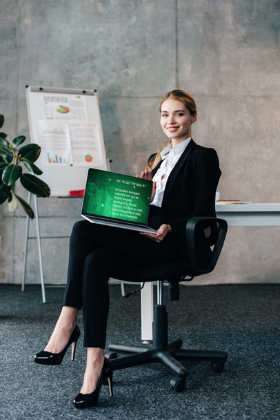Empresária sorridente atraente sentada na cadeira e segurando laptop com site médico na tela
 - Foto, Imagem