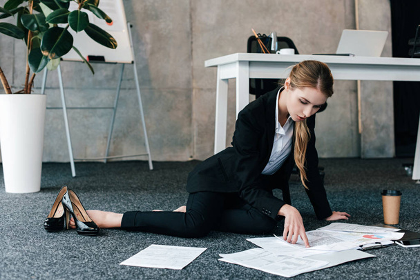 barefoot businesswoman sitting on floor near work-table and reading documents - Zdjęcie, obraz