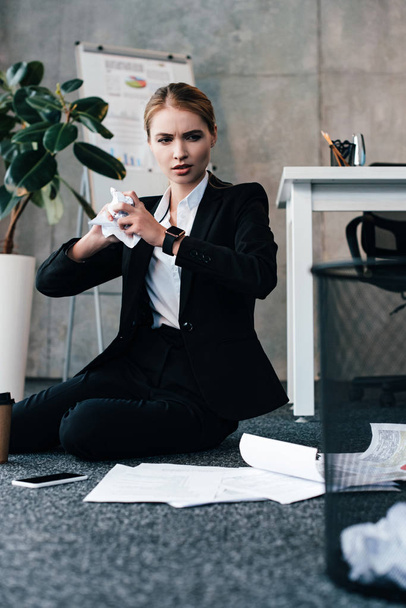 businesswoman sitting on floor and throwing crumpled papers to basket - Fotografie, Obrázek