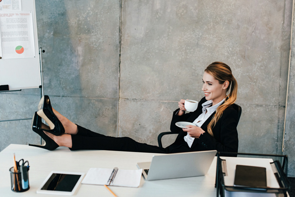 relaxed businesswoman with legs on table drinking coffee - Foto, afbeelding