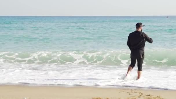 Ένας άντρας με ρούχα που βρίσκεται στην ακτή, ένα κρύο και κυματιστή θάλασσα - Πλάνα, βίντεο
