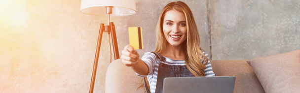 mulher bonita feliz mostrando cartão de crédito e sentado no sofá com laptop
 - Foto, Imagem