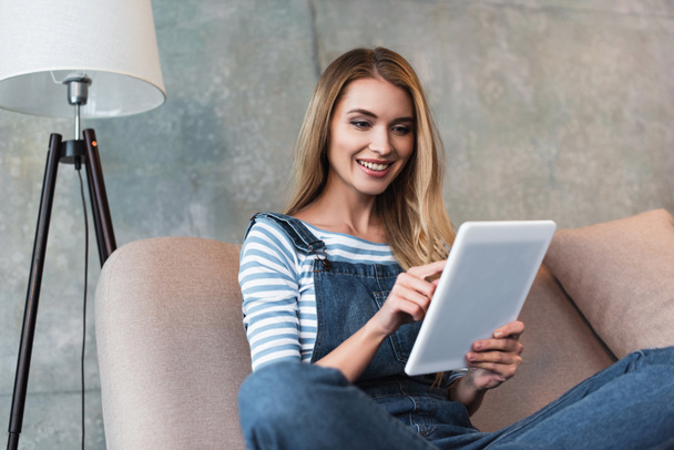 young woman sitting on pink sofa and using digital tablet - Foto, afbeelding