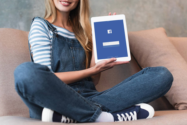 cropped view of young girl sitting on sofa and showing screen with facebook - Φωτογραφία, εικόνα