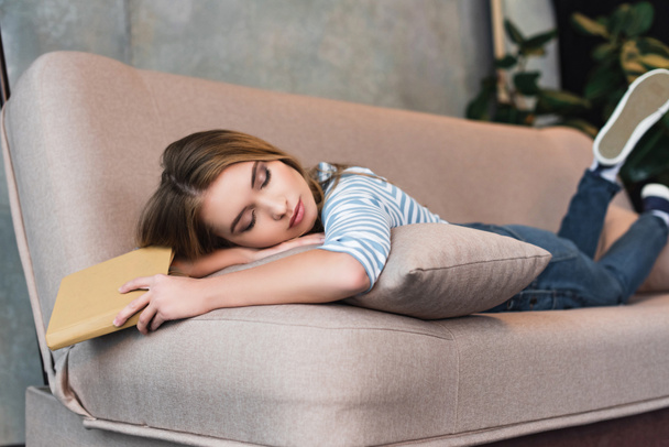 fiatal gyönyörű lány, pink kanapén alszik könyvvel a kezében, és átölelte a párna - Fotó, kép