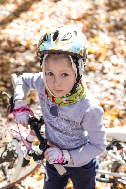 Cute little girl with a bicycle in the autumn forest. - Fotó, kép