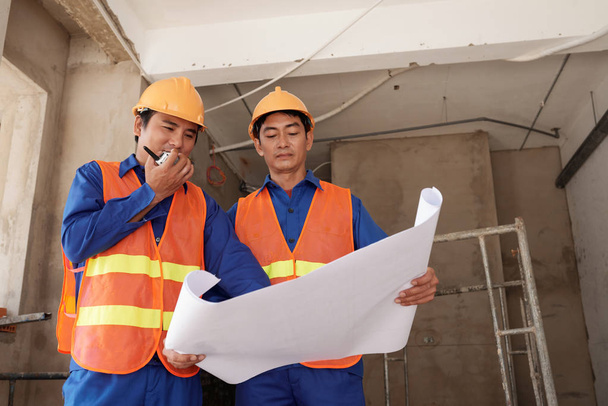 Aasialaiset rakennusinsinöörit keskustelevat suunnitelmasta työmaalla
 - Valokuva, kuva