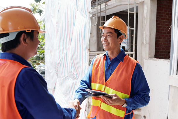 Lächelnder vietnamesischer Bauunternehmer trifft seinen neuen Mitarbeiter auf der Baustelle - Foto, Bild