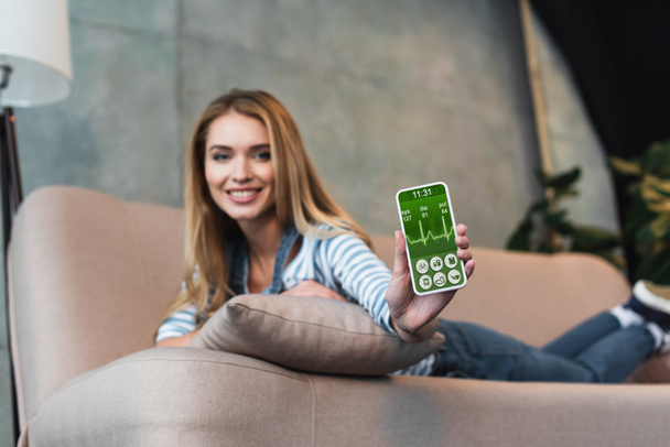 selective focus of smartphone with graphic in hand of woman on sofa - Foto, Bild