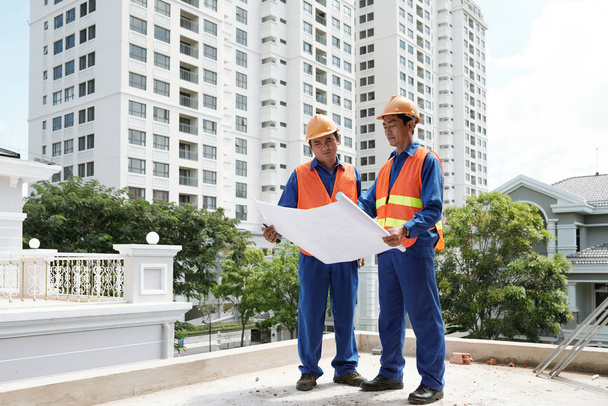 Вьетнамские инженеры-строители в униформе обсуждают план нового здания
 - Фото, изображение