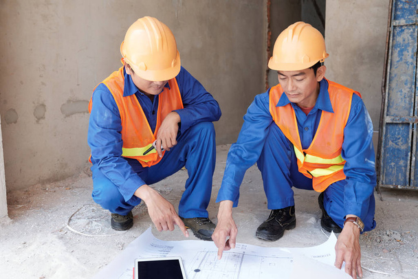 vietnamesischer Bauingenieur zeigt seinem Mitarbeiter auf der Baustelle den Bauplan - Foto, Bild