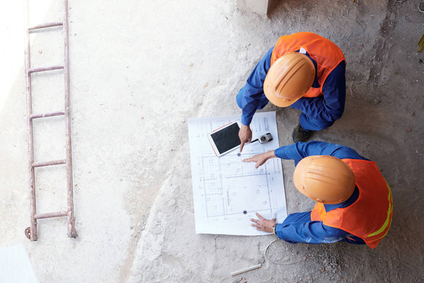 Bauunternehmer zeigt seinem Mitarbeiter den Bauplan der Wohnung, Blick von oben - Foto, Bild