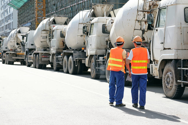 Contractor discussing supply of cement with coworker near line of trucks - Photo, Image