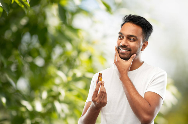 smiling indian man applying grooming oil to beard - Фото, изображение