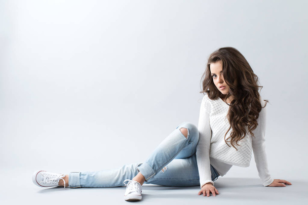 Woman sitting on floor isolated over gray background. Girl with long wavy hair. - Fotoğraf, Görsel
