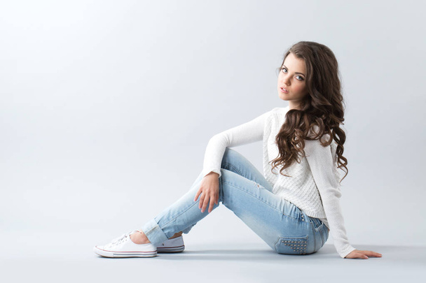 Woman sitting on the floor on gray background. Girl with long wavy hair. - Zdjęcie, obraz