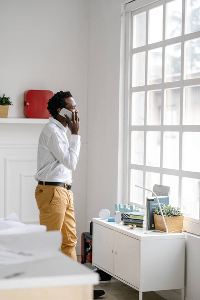 Handsome African stylish businessman standing at his office and talking on cell phone. - Foto, imagen