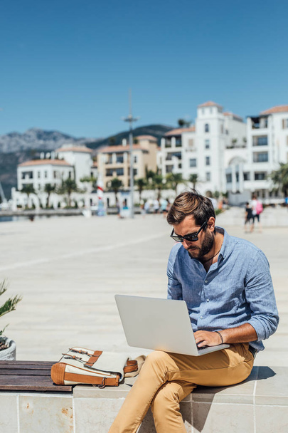 Handsome Caucasian man freelancer sitting on bench and working on his laptop. - 写真・画像