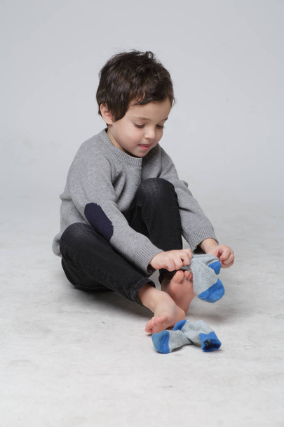 Πορτρέτο του χαριτωμένο μικρό παιδί κάθεται εκμάθηση πώς να θέσει τις κάλτσες από αυτόν αυτο, ευχαρίστως Toddler αγόρι τράβηγμα κάλτσες του στο πόδι του, η έννοια της ανάπτυξης του παιδιού - Φωτογραφία, εικόνα