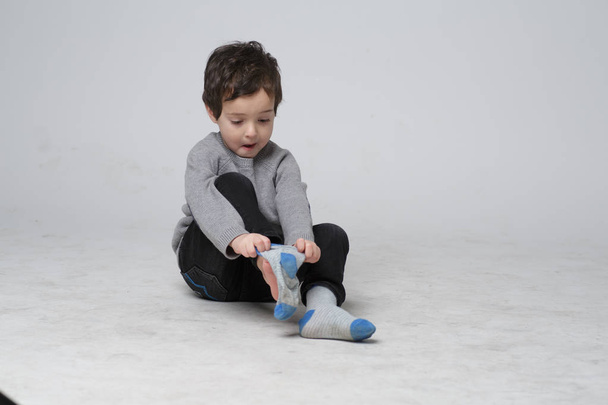 Porträt eines niedlichen kleinen Kindes, das lernt, wie man die Socken selbst anzieht, fröhlicher Kleinkind-Junge, der seine Socken bis zum Fuß zieht, Entwicklungskonzept des Kindes - Foto, Bild
