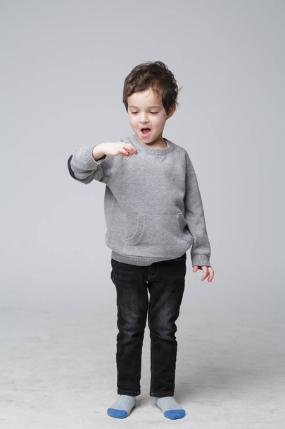 Young emotional handsome boy standing on grey studio background. Human emotions, facial expression concept. - Photo, Image