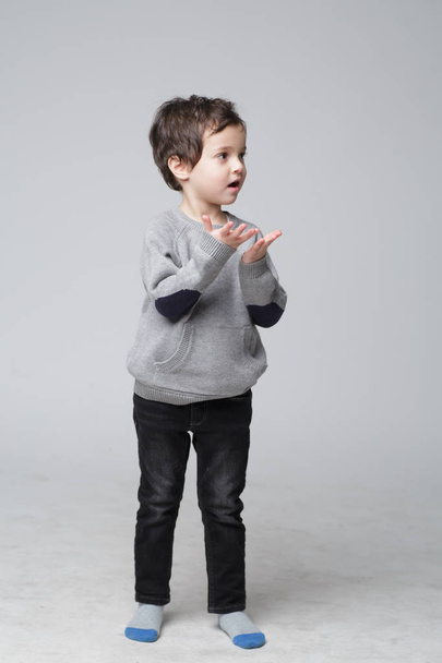 Young emotional handsome boy standing on grey studio background. He looks in the palm of his hand. Child hygiene concept, health care during a pandemic, Human emotions, facial expression.Human emotions, facial expression. - Foto, afbeelding