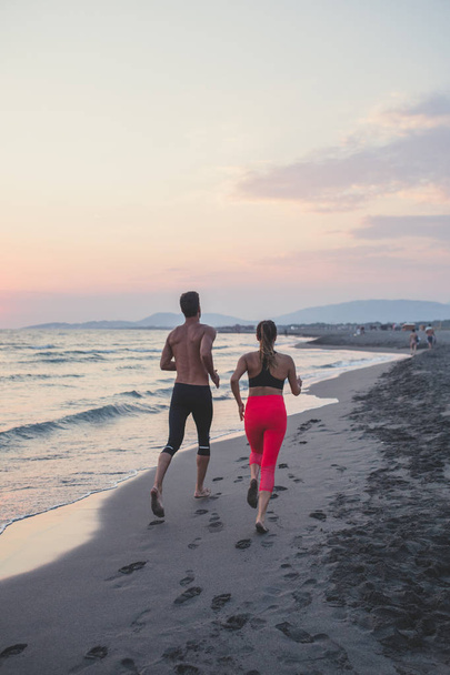 Back view of sportsman and sportswoman running by the ocean. - Foto, immagini