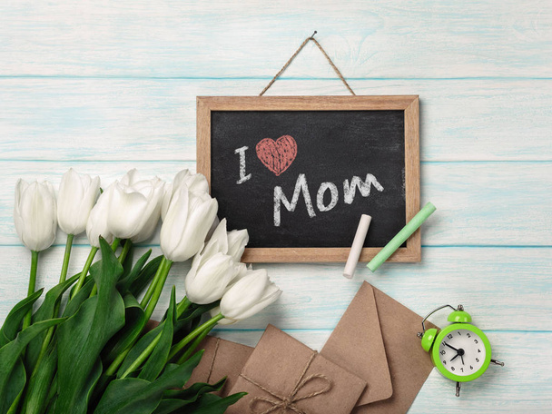 Een boeket van witte tulpen met krijt-bestuur en enveloppen op blauwe houten planken. Bovenaanzicht met plaats voor uw gelukwensen. Mother's day. - Foto, afbeelding