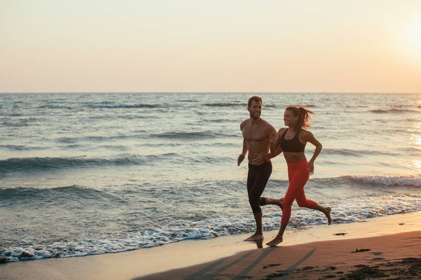 Handsome Caucasian man and beautiful woman running on sandy beach in sunset. - Photo, image