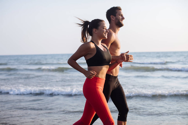 Handsome Caucasian man and beautiful woman running on sandy beach. - Фото, зображення