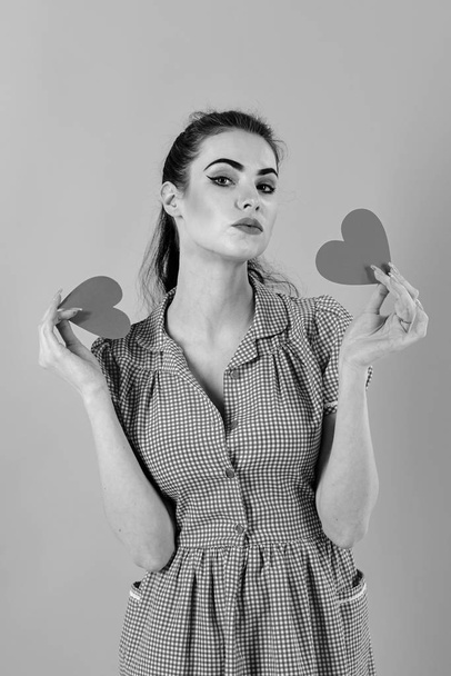 Dating, relationship, beauty concept. Girl smiles with valentine hearts isolated on pink. Girl with serious face, make up and red hearts. Woman in stylish dress holds romantic symbols. Full of love - Фото, зображення